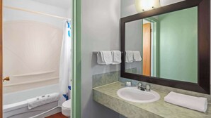 A bathroom with a bathtub, toilet, sink, and a large mirror. - Travelodge by Wyndham Grand Falls (St. Andre)
