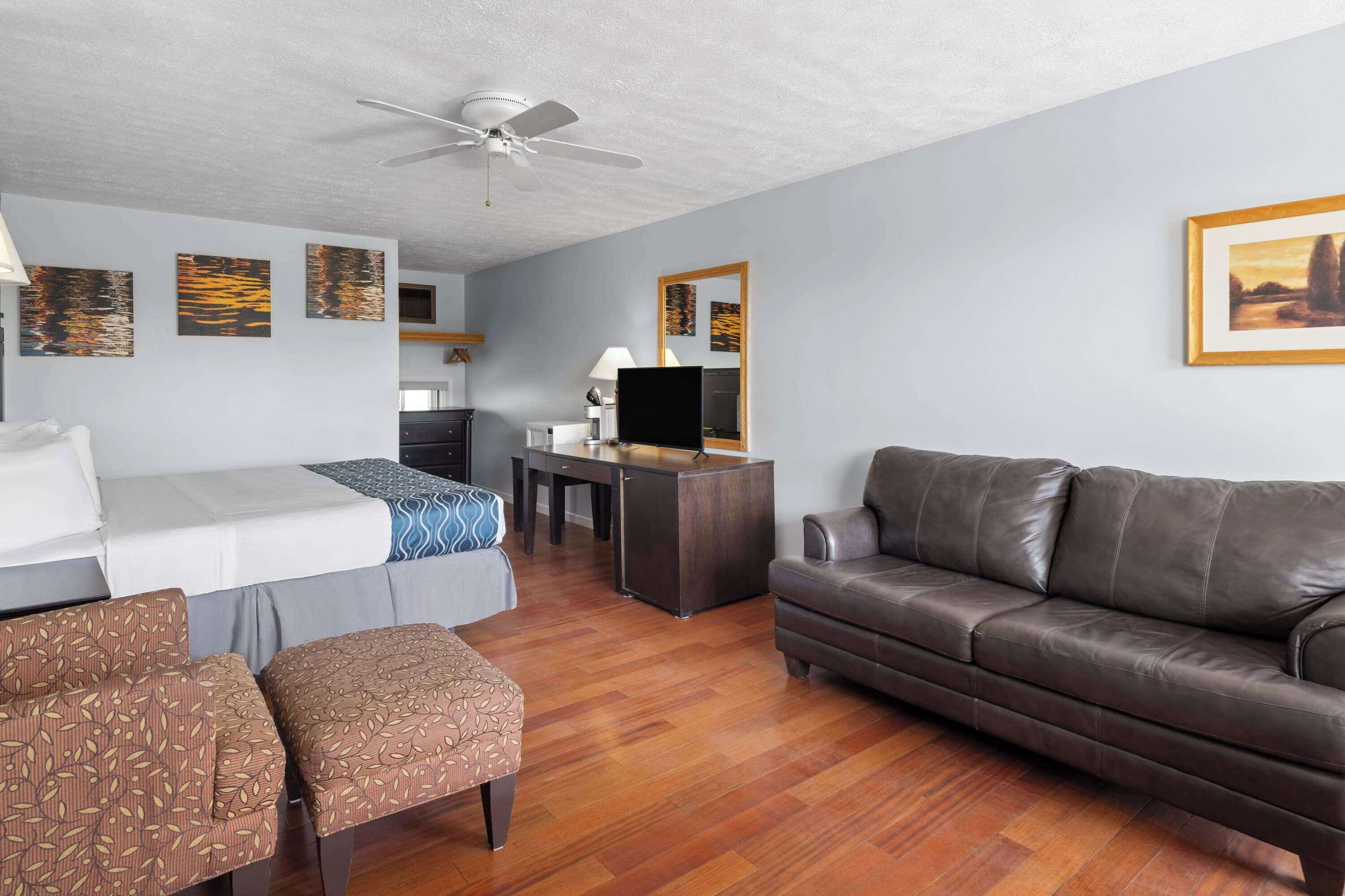 A hotel room with a bed, a sofa, a desk with a TV, and artwork on the walls.