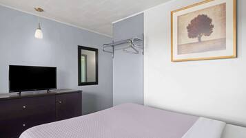 Quarto com cama, cómoda, televisão, porta-toalhas fixado na parede e um quadro emoldurado.