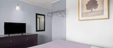 Un dormitorio con cama, cómoda, televisor, toallero en la pared y un cuadro enmarcado.
