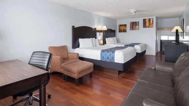 A hotel room with two beds, a desk, a chair, a sofa, and a ceiling fan. - Travelodge by Wyndham Grand Falls (St. Andre)