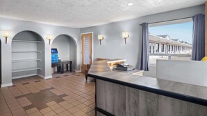 A hotel lobby with a reception desk, a computer, a seating area, and a view of the beach. - Travelodge by Wyndham Grand Falls (St. Andre)
