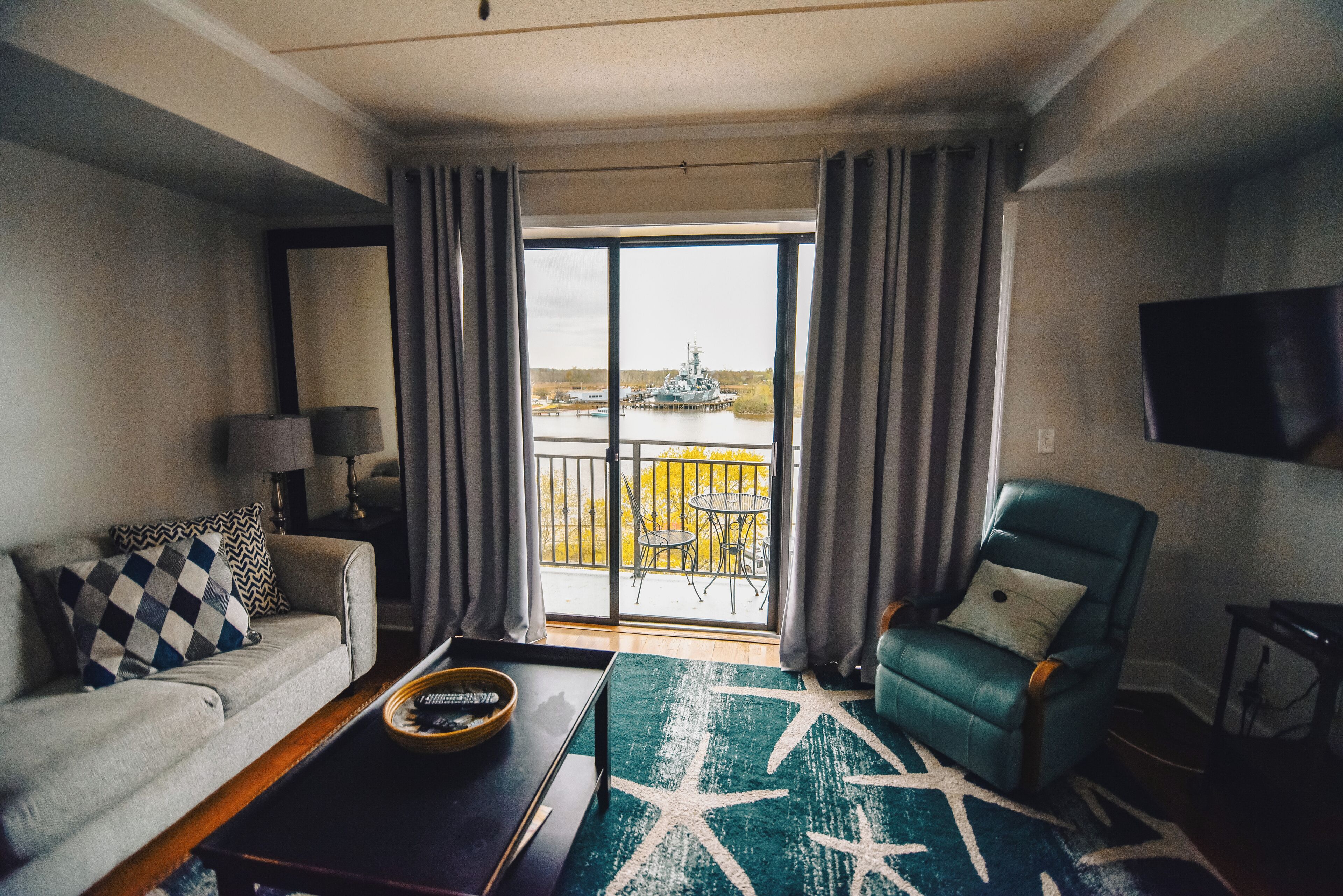 Uma sala de estar com sofá, poltrona, mesa de centro e vista para a água através de uma grande janela.