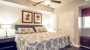 A bedroom with a bed, a ceiling fan, a nightstand, a lamp, framed artwork, and a door.