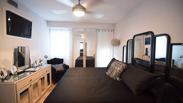 A hotel room with a large bed, bedside tables, a desk with a mirror, a ceiling fan, and a TV mounted on the wall.