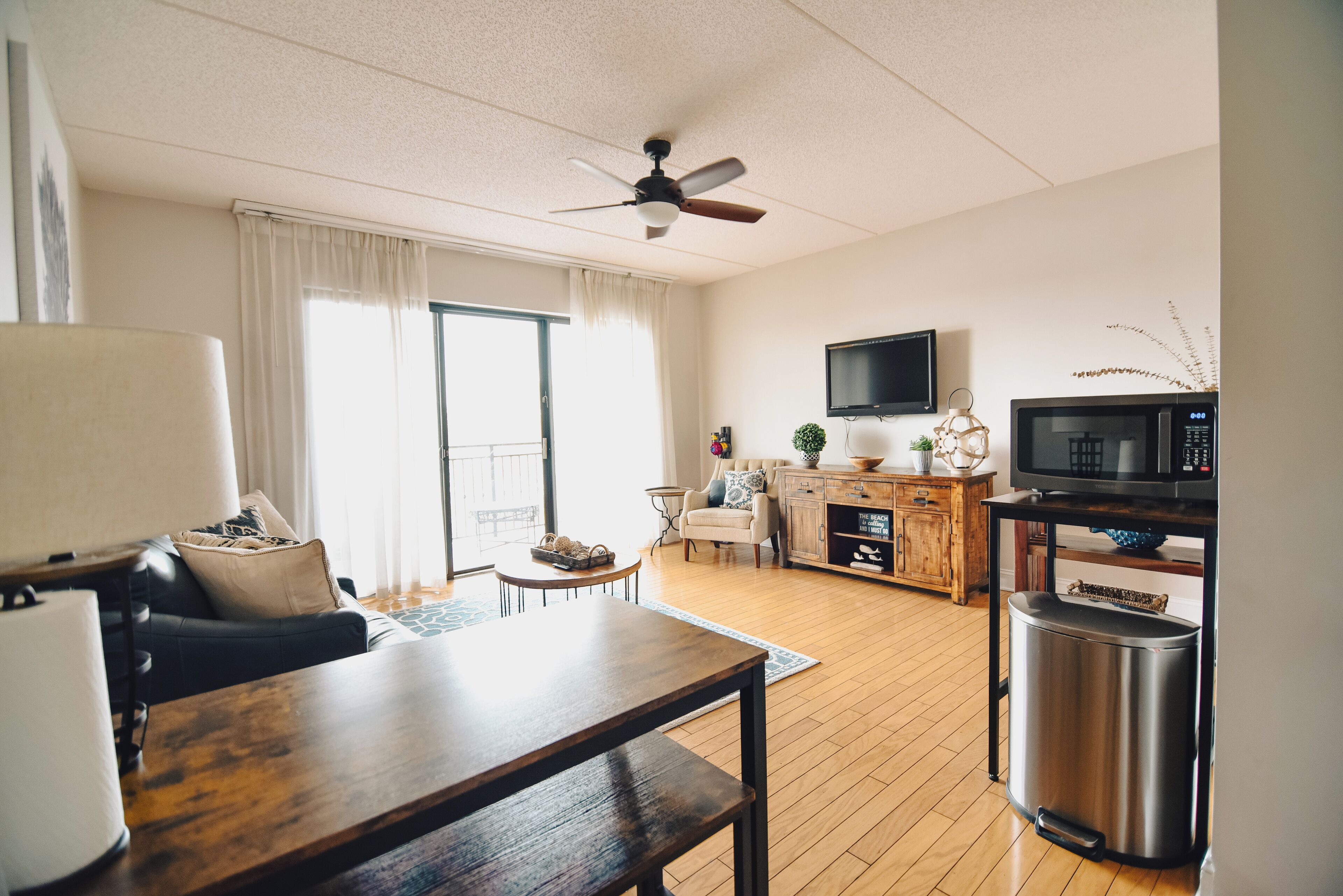 Un salon moderne comprenant un canapé, une table basse en bois, un téléviseur et un coin cuisine avec un four à micro-ondes.