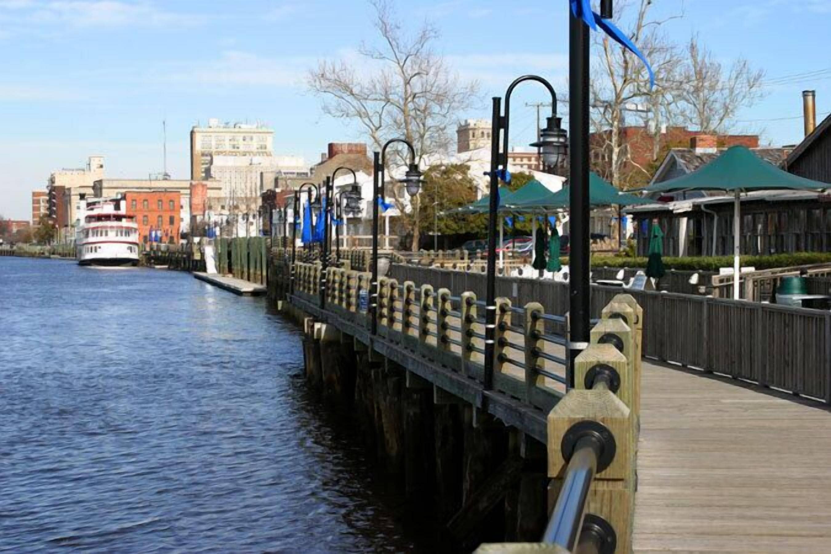 A waterfront promenade with a wooden walkway, metal railings, and a boat docked on the water.