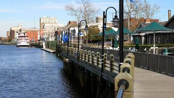 A waterfront promenade with a wooden walkway, metal railings, and a boat docked on the water.
