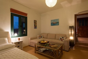 A cozy living room with a sofa, a coffee table with a chessboard, a lamp, and a painting of a boat on the wall. - The Hillside Home (Platanias)