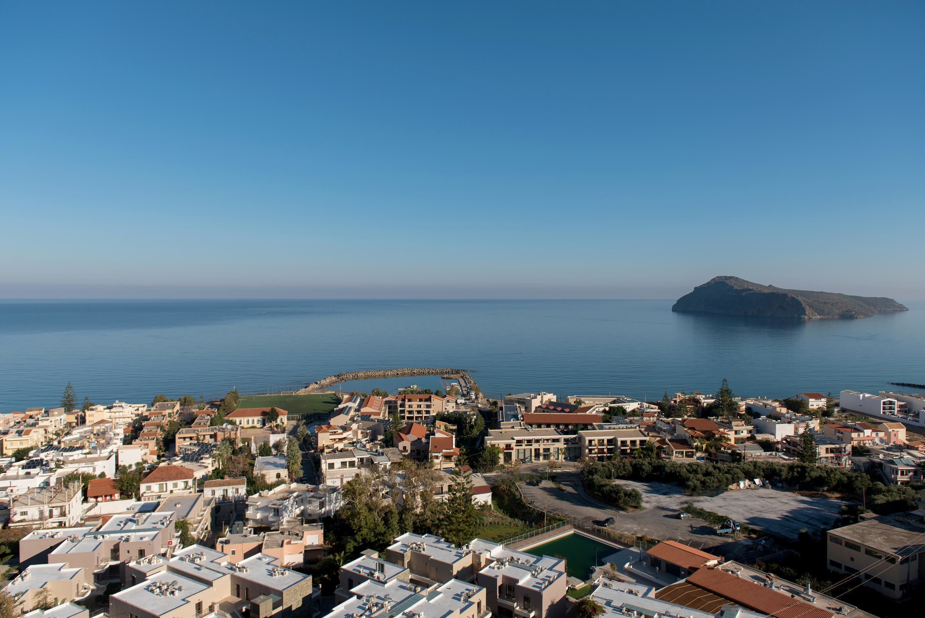 Une ville côtière avec des bâtiments, un ciel dégagé et une île visible au loin.