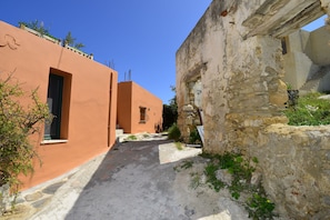 A narrow alleyway with a stone wall on one side and a building with a door and window on the other. - The Hillside Home (Platanias)
