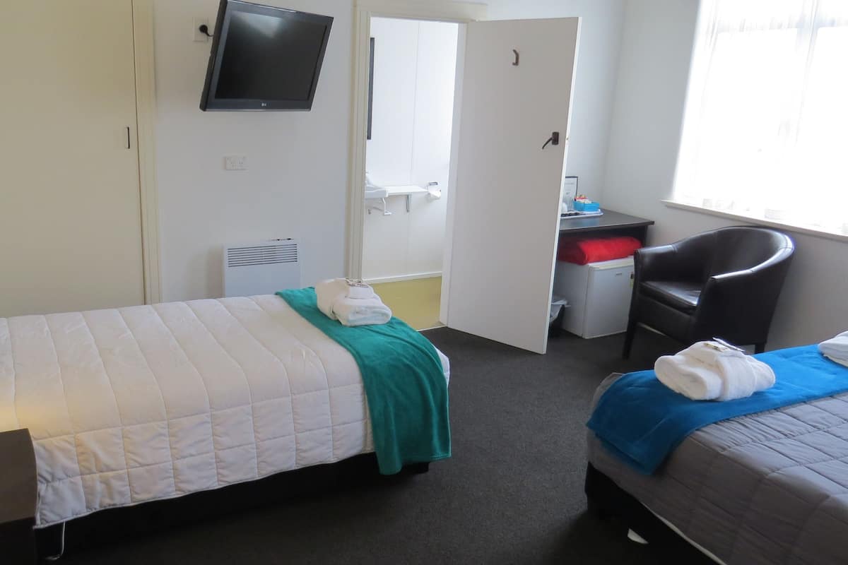 A hotel room with two beds, a desk, a chair, a TV, and a window.