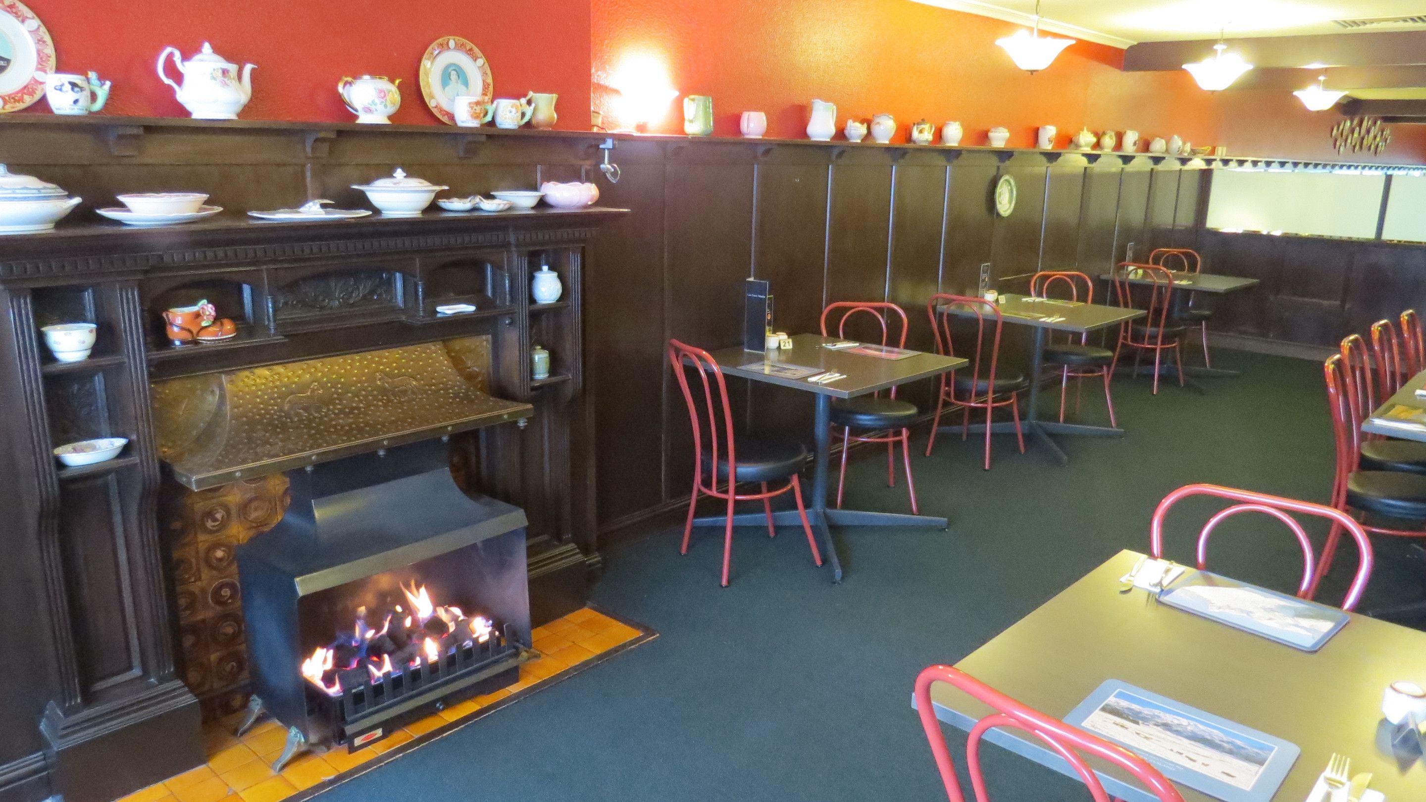 Un restaurante con chimenea, mesas, sillas y una variedad de platos expuestos en estanterías.