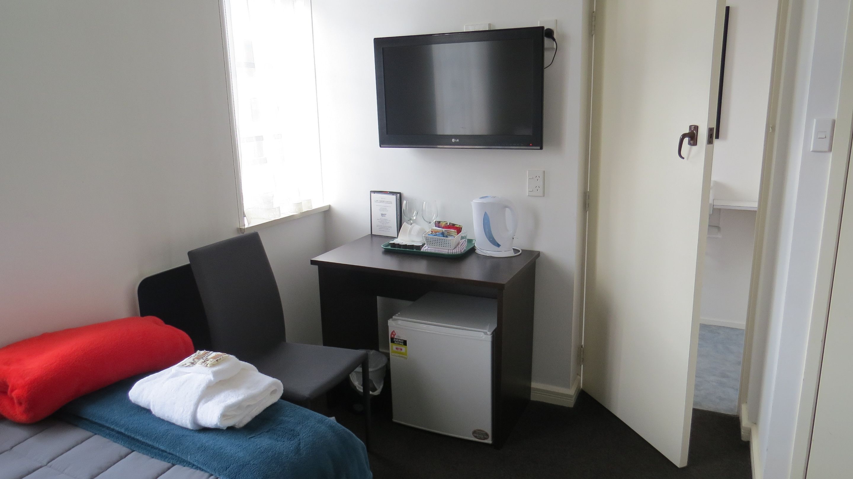 A hotel room with a bed, a desk with a television, a small refrigerator, and a kettle.