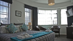 A hotel room with a large bed, two chairs, a desk, and a television. - Law Courts Hotel (Dunedin)