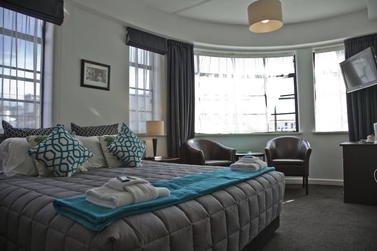 A hotel room with a large bed, two chairs, a desk, and a television.