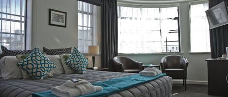 A hotel room with a large bed, two chairs, a desk, and a television.