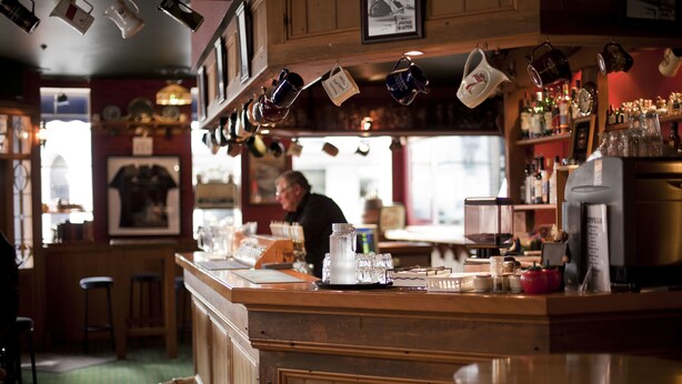 A bar area with wooden counters, hanging mugs, and various bottles. - Law Courts Hotel (Dunedin)