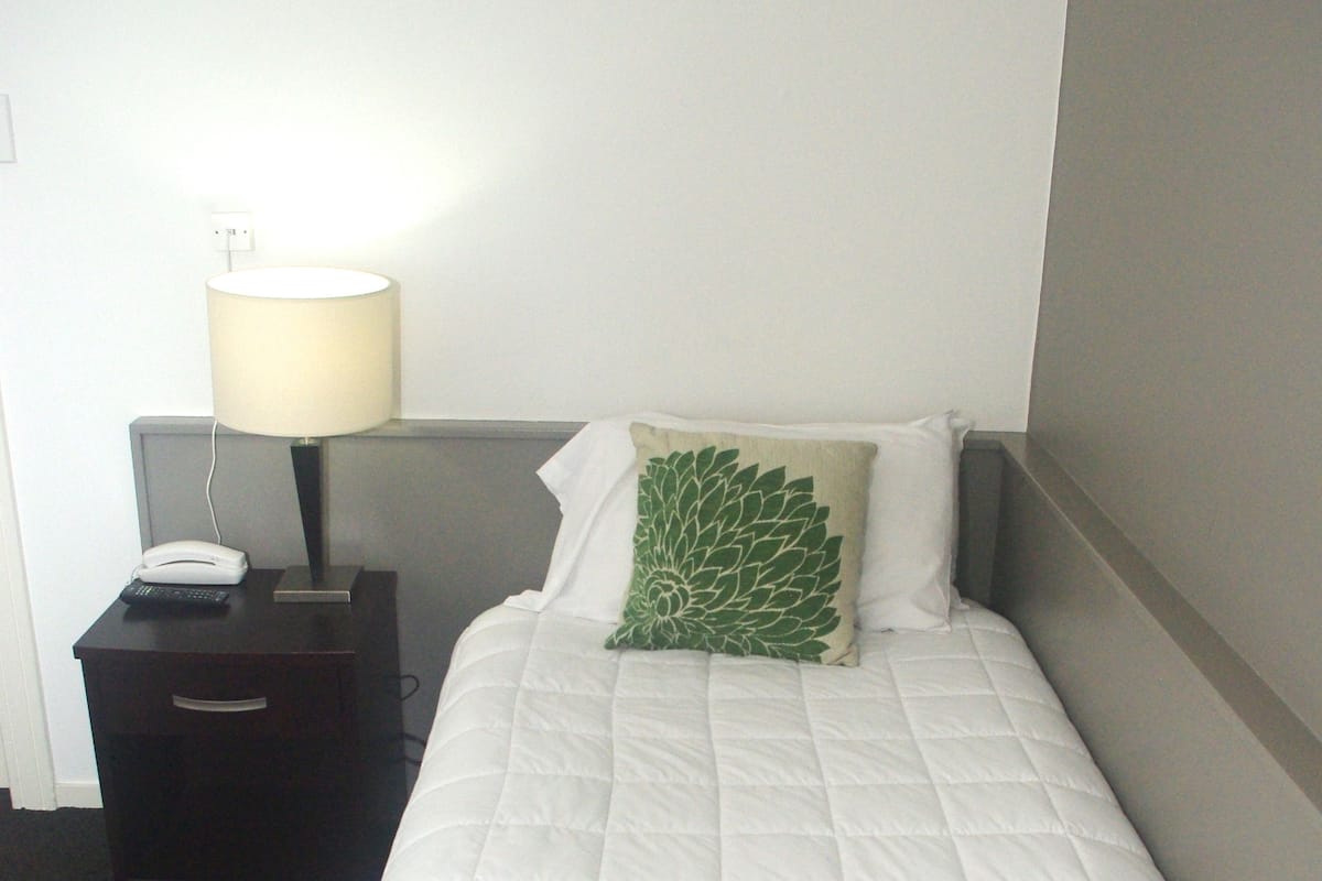 A neatly made bed with a green throw blanket and a white pillow.