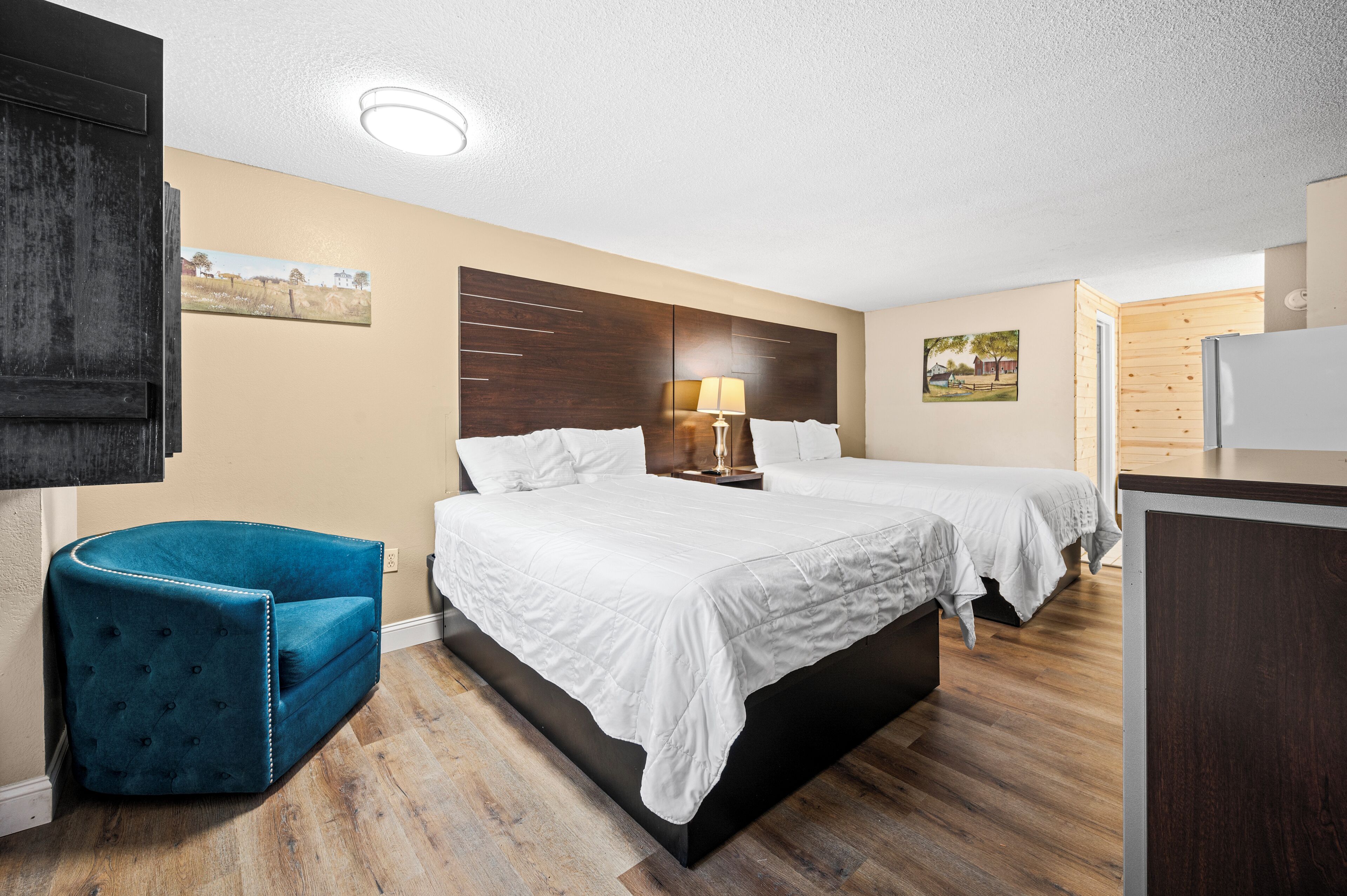 Habitación de hotel con una cama grande, una mesita de noche con lámpara, un sillón azul y un armario de madera.