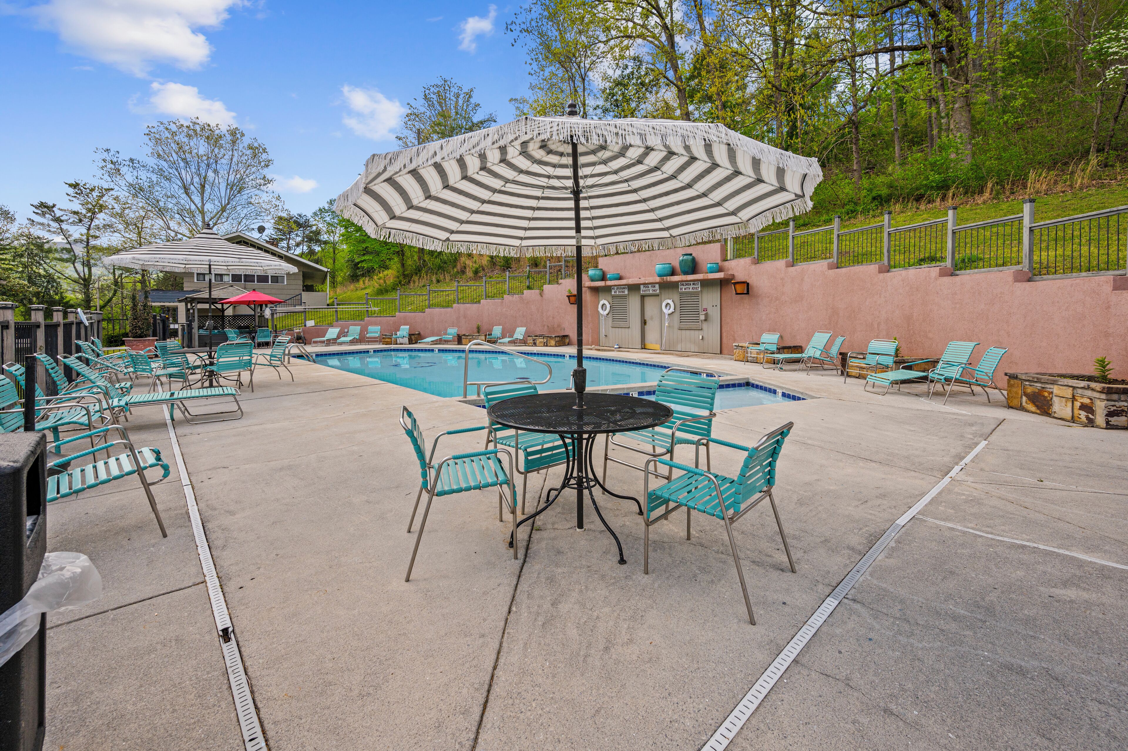 A pool area with lounge chairs and a table under a striped umbrella.