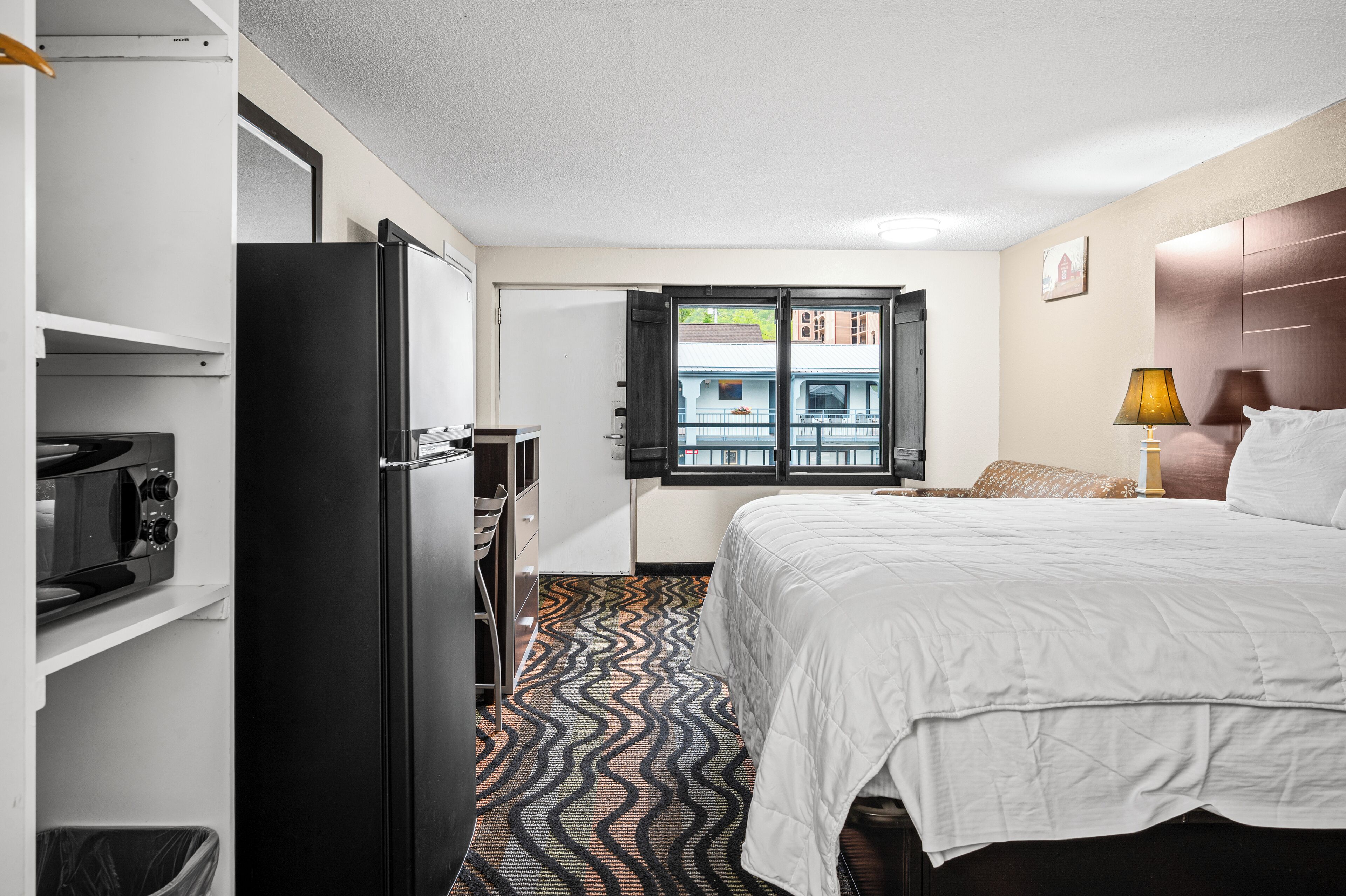 Habitación de hotel con cama, escritorio, refrigerador, microondas y ventana con vistas a edificios.