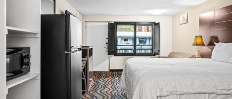 Habitación de hotel con cama, escritorio, refrigerador, microondas y ventana con vistas a edificios.