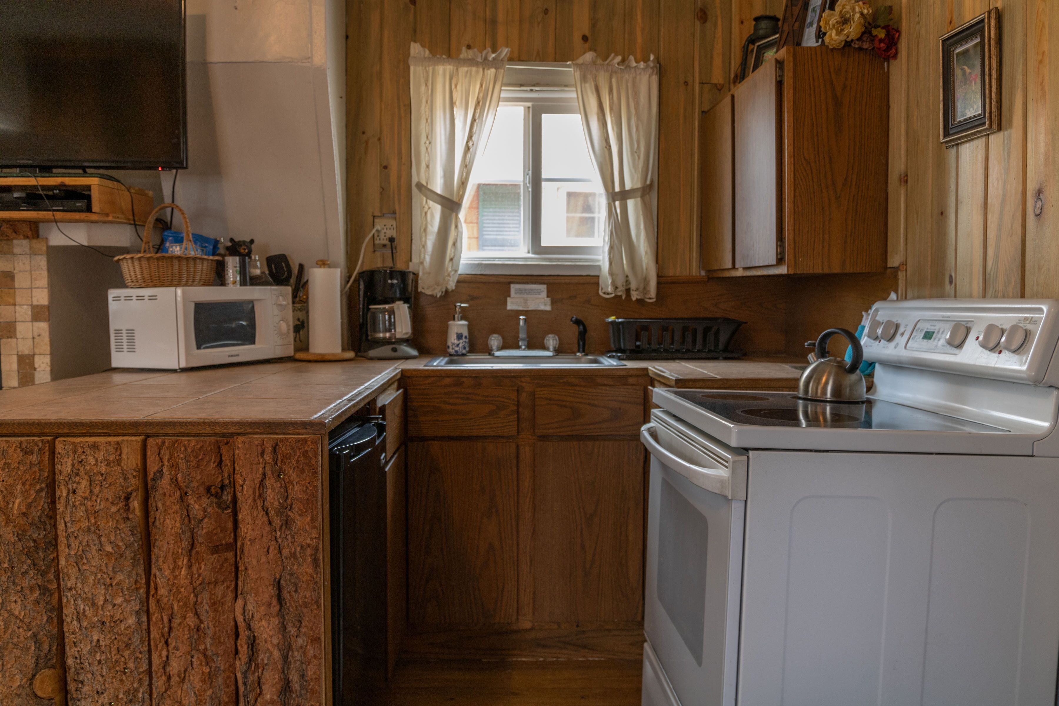 A compact kitchen with wooden cabinets, a microwave, a kettle, and a sink.