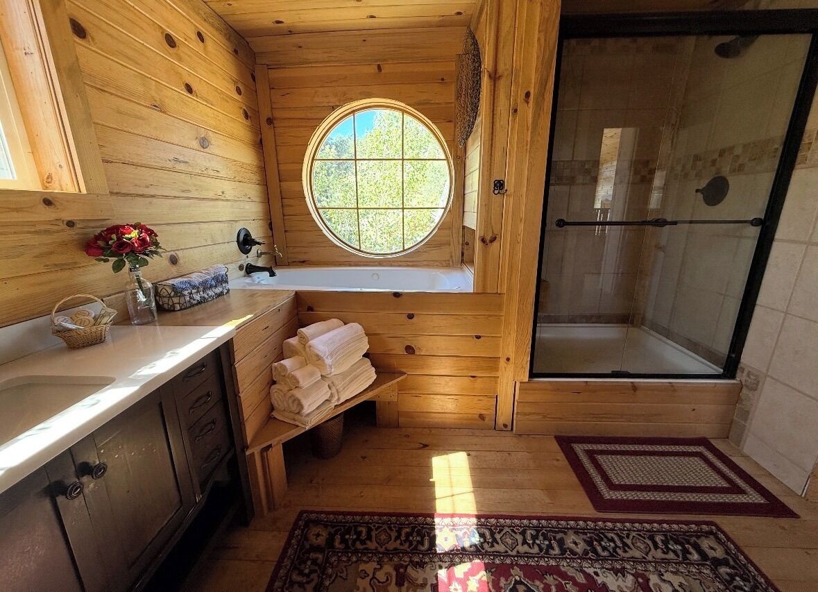 A wooden cabin bathroom with a window, a shower, and a sink.