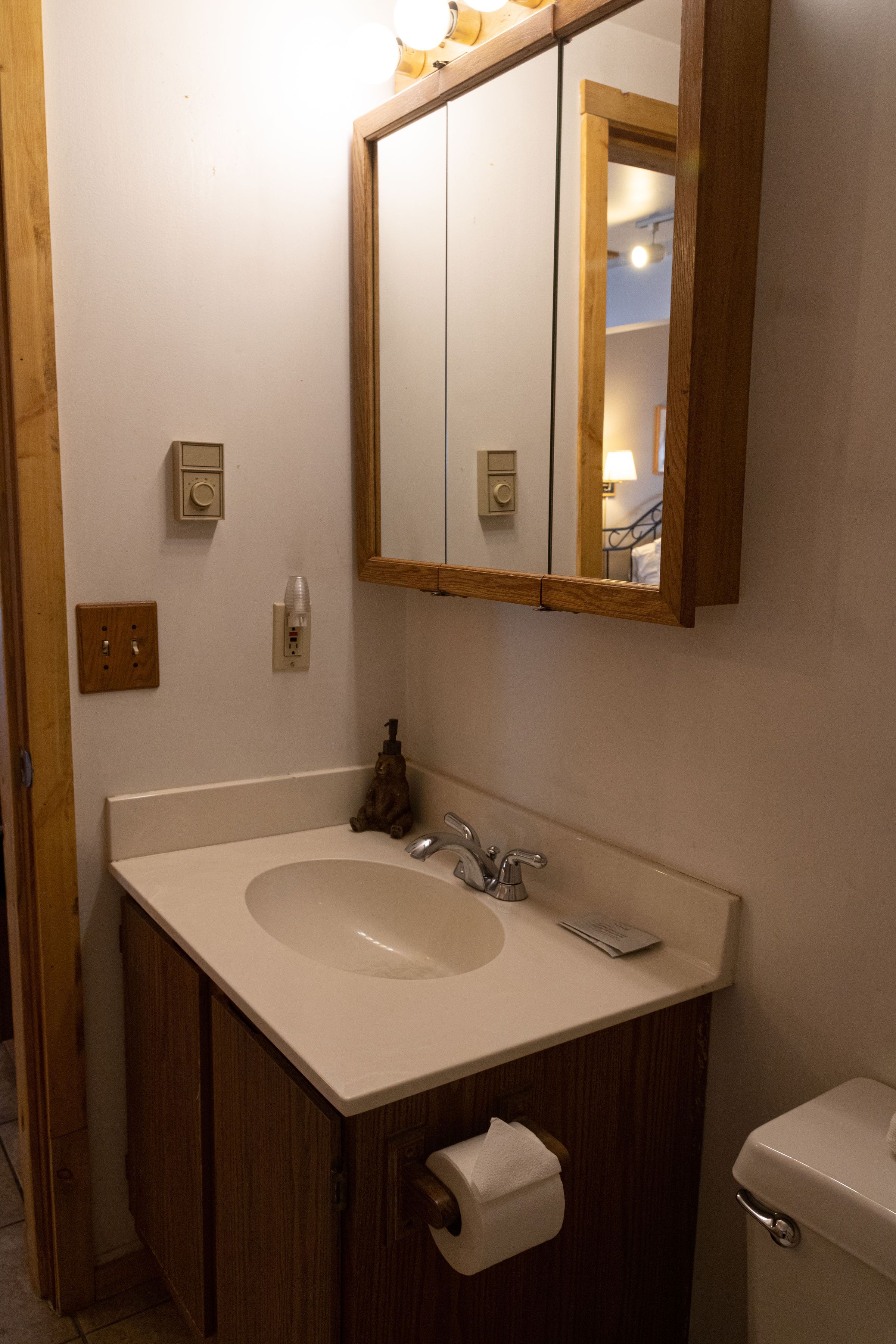 A bathroom with a wooden vanity, a sink, a toilet, and a mirror.