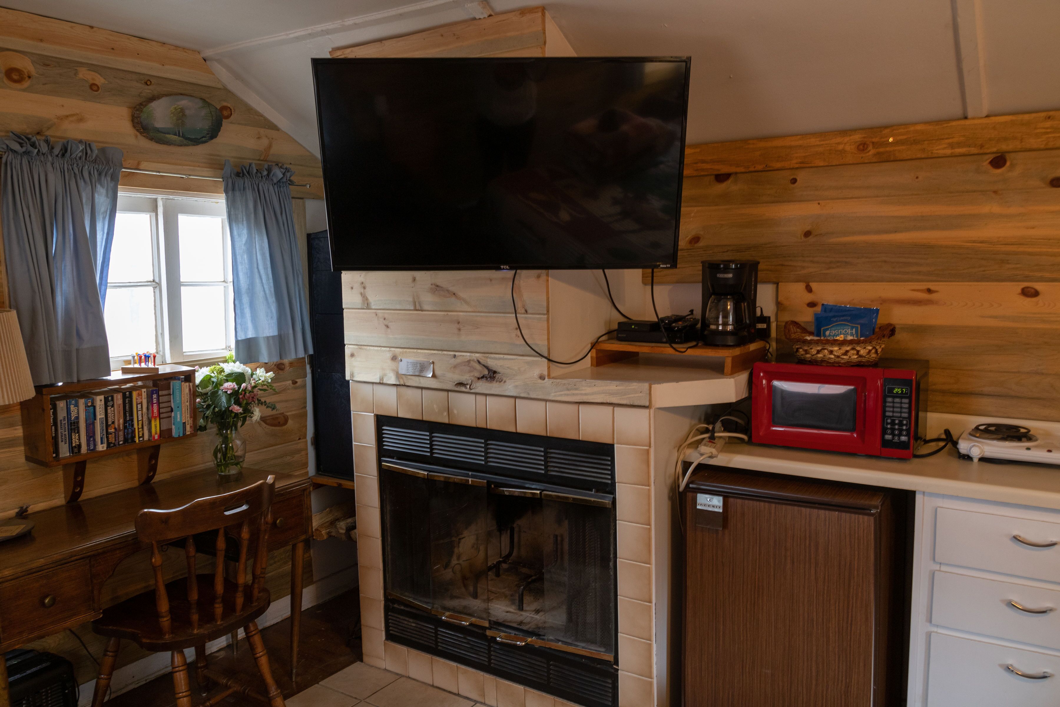 A cozy living room with a fireplace, a television mounted above it, a bookshelf, and a microwave on the counter.