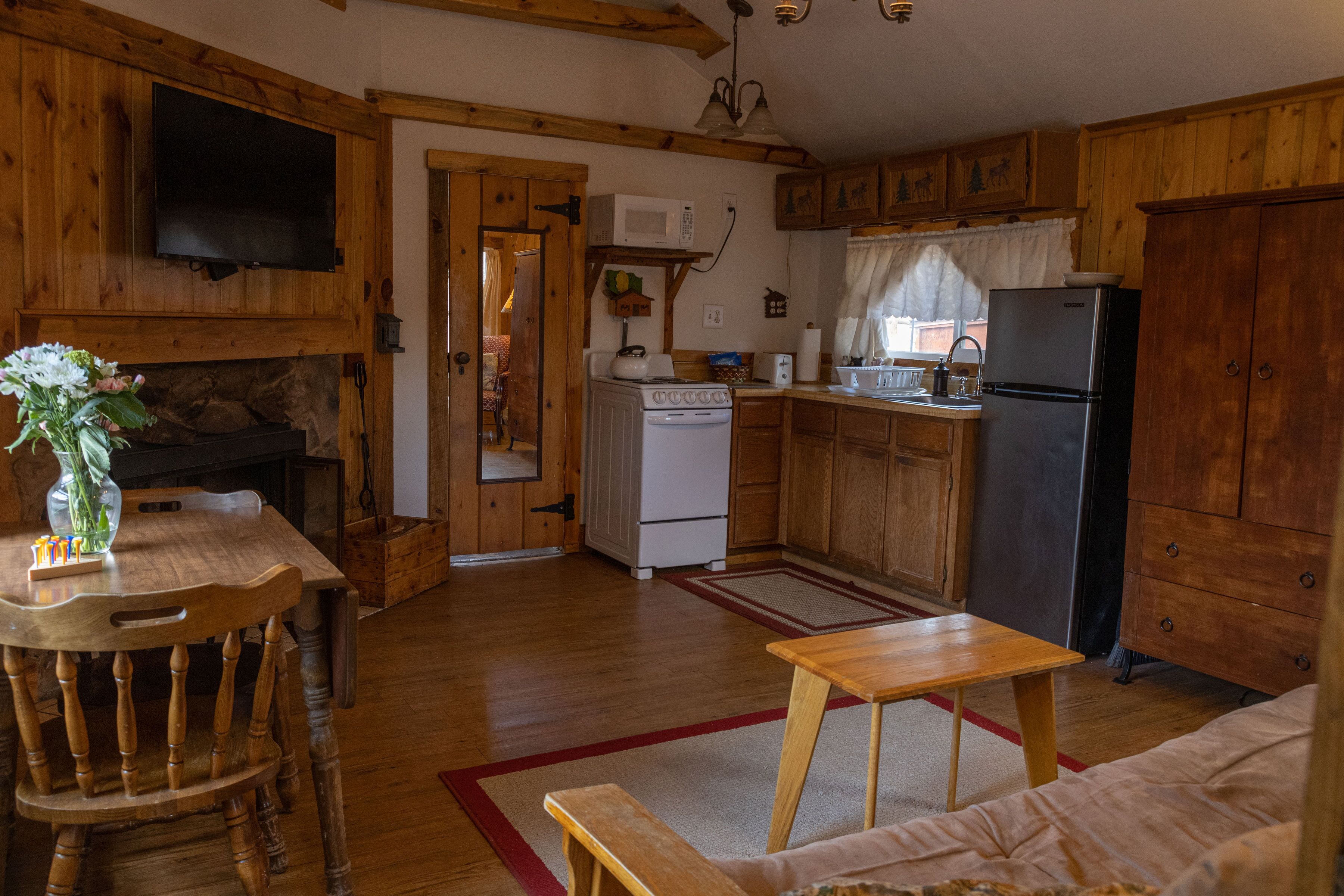 A wooden cabin interior with a dining area, kitchen, and a cozy living space.
