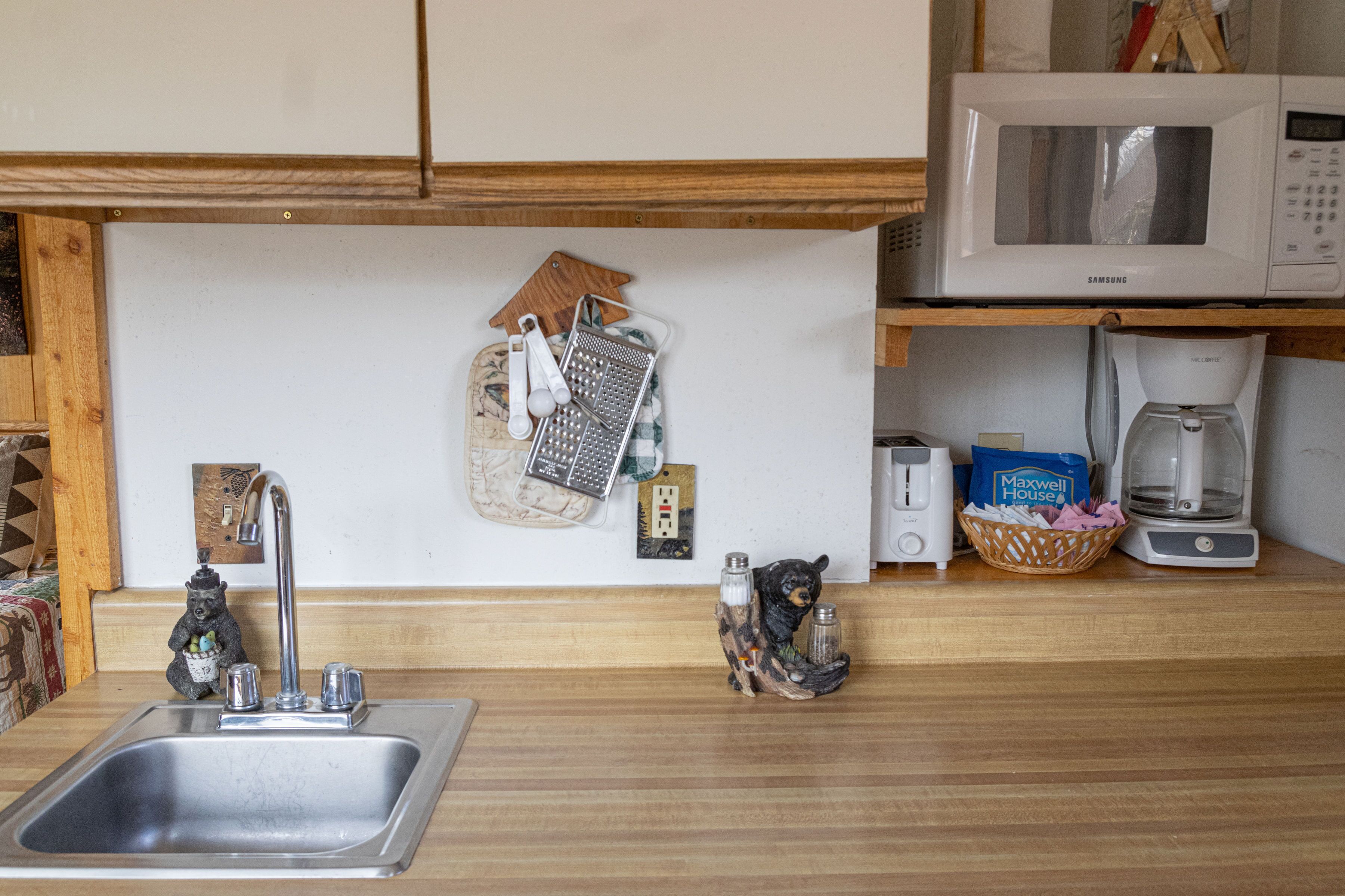 A kitchen with a stainless steel sink, a microwave, a coffee maker, and a bear-shaped salt and pepper shaker.
