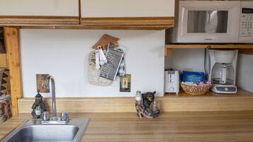 A kitchen with a stainless steel sink, a microwave, a coffee maker, and a bear-shaped salt and pepper shaker.