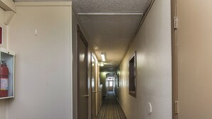 A hotel hallway with doors on both sides, a fire extinguisher on the left, and a light fixture on the ceiling. - Relax Inn (Manor)