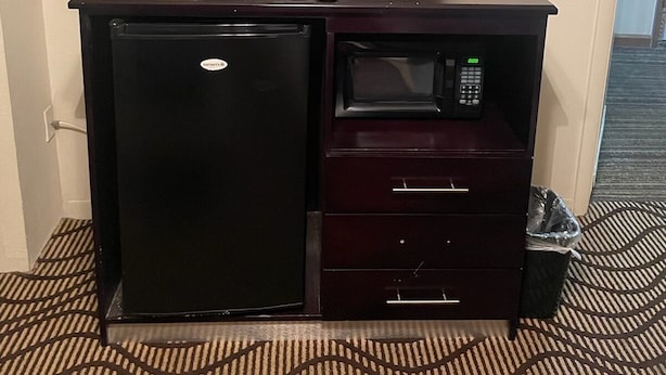A compact kitchenette with a refrigerator, microwave, and a flat-screen TV. - Relax Inn (Manor)