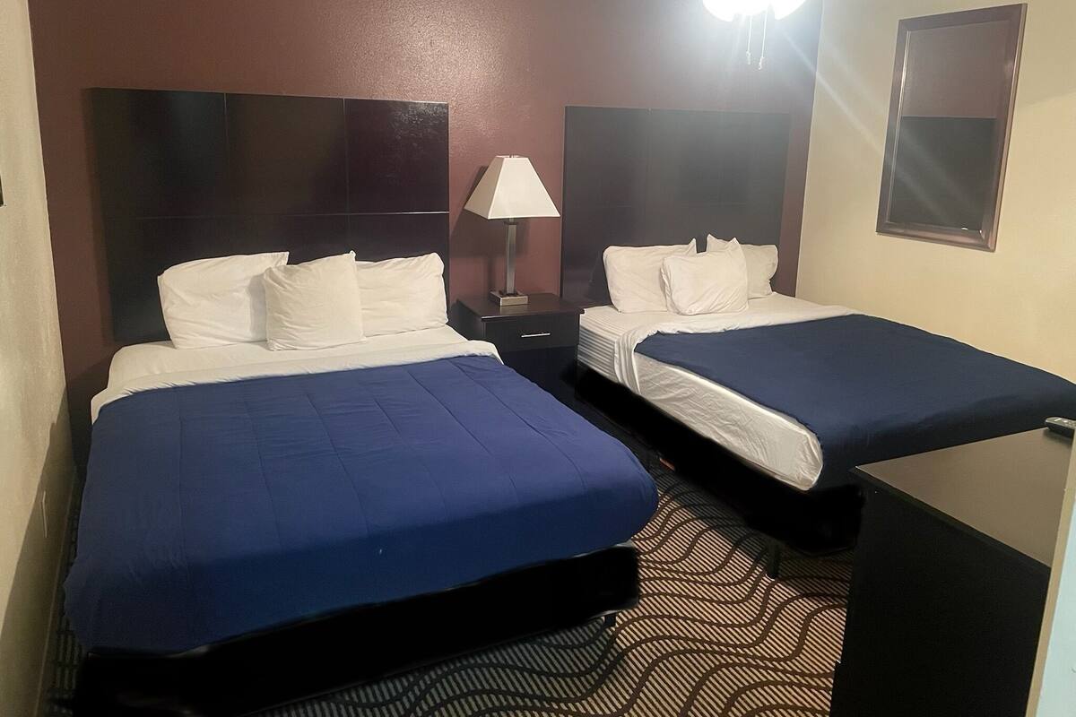 A hotel room with two beds, a nightstand, a lamp, and a ceiling fan.