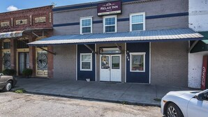 A two-story building with a sign for 'Relax Inn' indicating daily and weekly availability. - Relax Inn (Manor)
