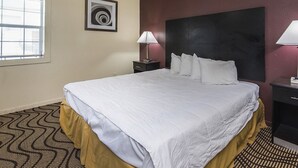 A hotel room with a bed, a ceiling fan, a nightstand, a lamp, a framed picture, and a window with blinds. - Relax Inn (Manor)