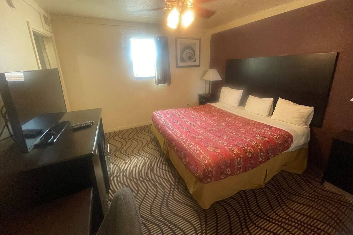 A hotel room with a bed, a desk with a computer, a ceiling fan, and a window.