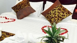 A neatly made bed with white linens and decorative pillows, a tray with fruits and drinks, and a wooden headboard. - Summer Palace Hotel (Yangon)