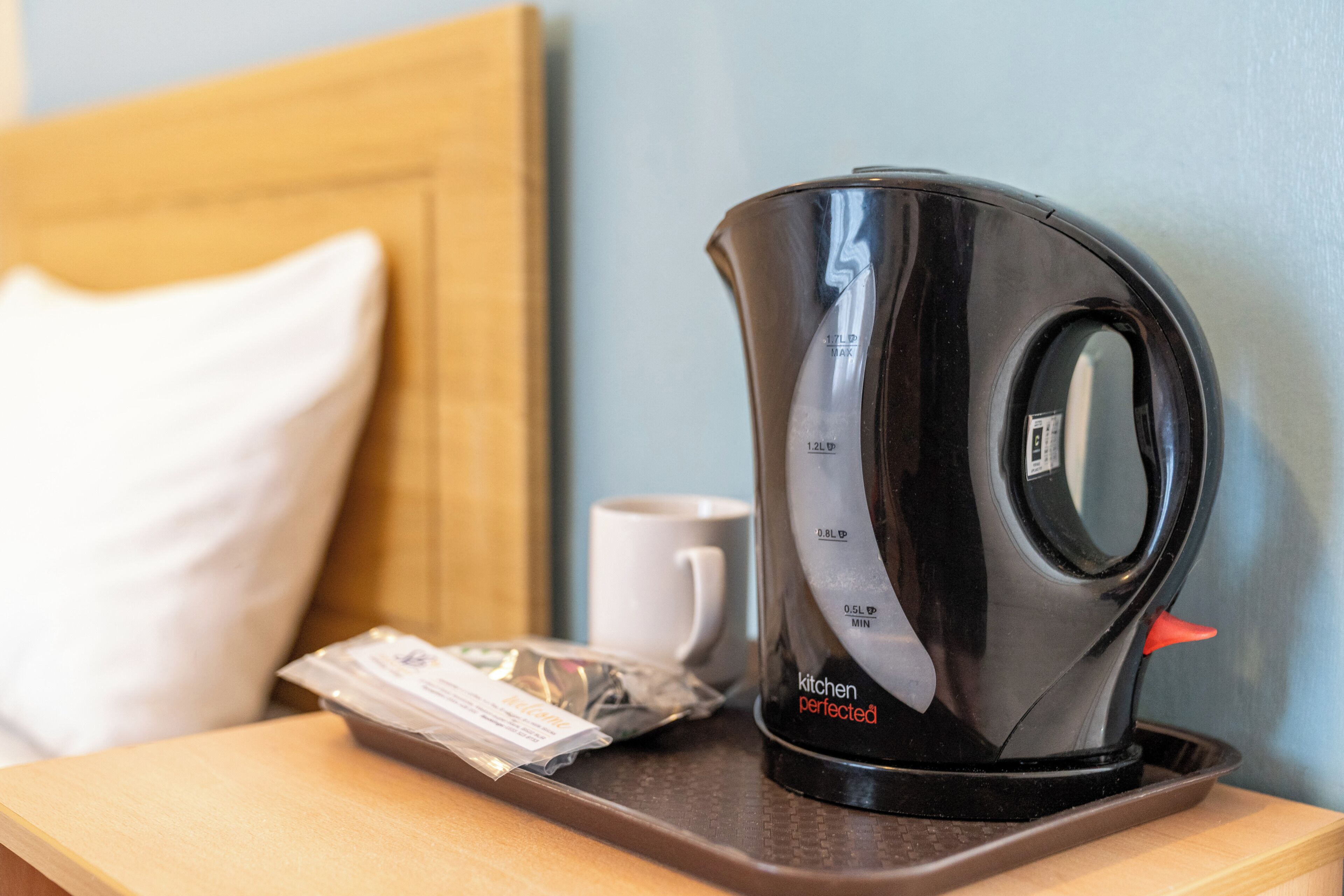 A black electric kettle on a tray with a packet of tea and a white mug on a wooden table.