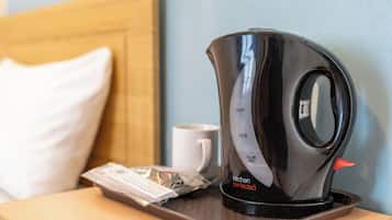 A black electric kettle on a tray with a packet of tea and a white mug on a wooden table.