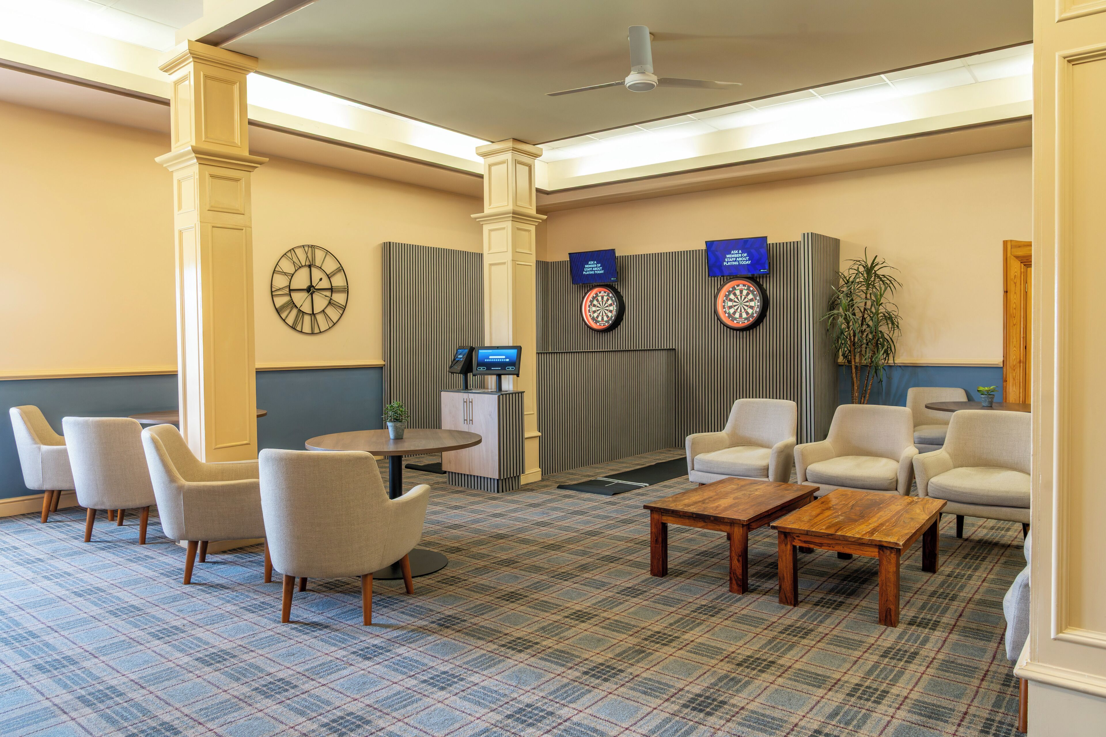 Eine Lobby mit Schachbrettmuster-Teppich, einer Sitzecke mit Stühlen, einem Empfangstresen, einer Uhr und Dartspielen.