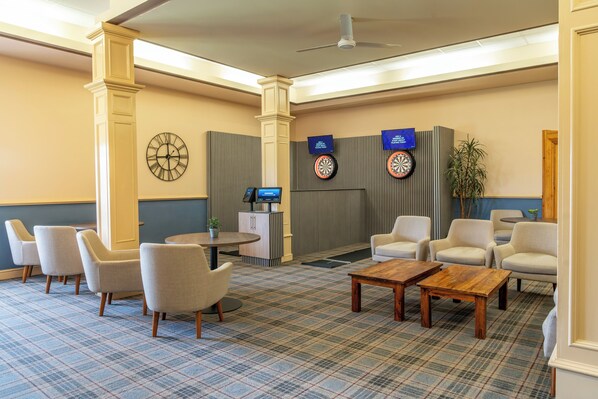 A lobby with a checkered carpet, seating area with chairs, a reception desk, a clock, and dartboards.