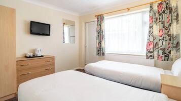 A hotel room with two beds, a flat-screen TV, a wooden dresser, and a window with floral curtains.