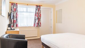 A hotel room with a bed, a desk with a computer, a chair, a radiator, and curtains.
