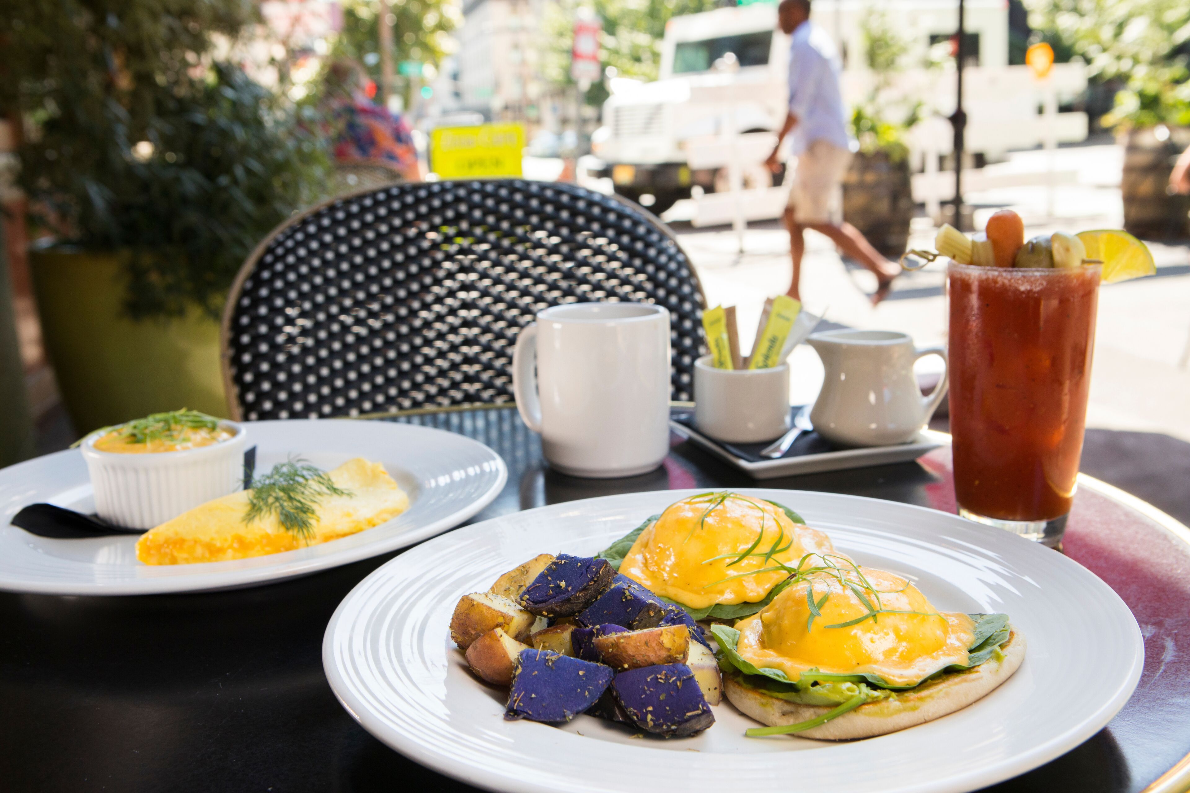 Una tavola imbandita con piatti da colazione, tra cui uova alla Benedict e un Bloody Mary.