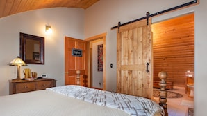 Une chambre à coucher comprenant un lit, une commode, une lampe, un miroir et une porte coulissante en bois donnant sur une salle de bain.