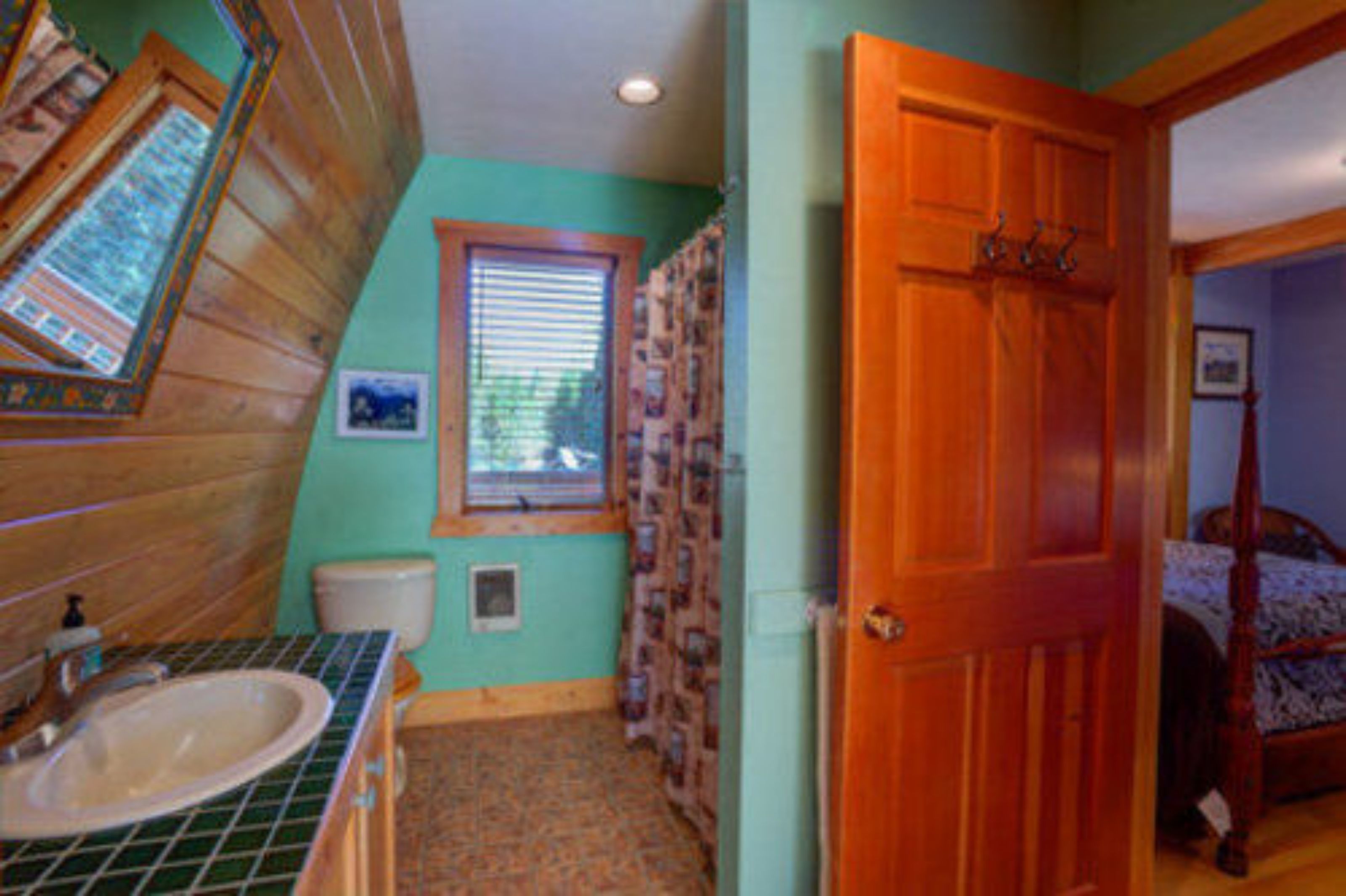 Une salle de bain avec un meuble-lavabo en bois, des toilettes et une fenêtre avec des stores.